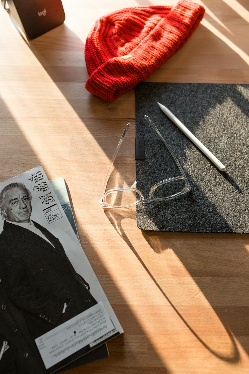 Red beanie, eyeglasses, and speaker on a wooden desk.