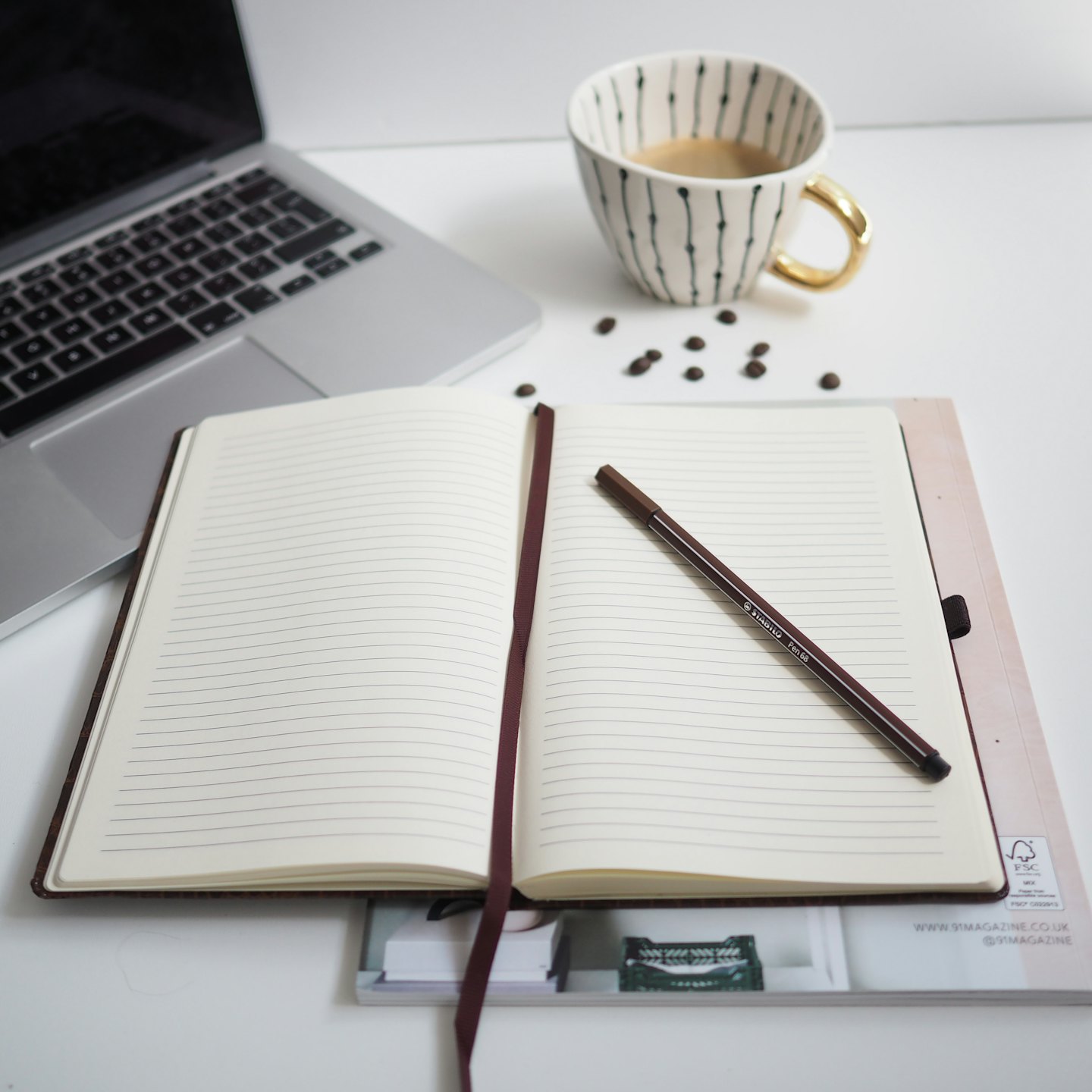 Overhead view of a minimalist desk with a laptop, notebook, and coffee cup.