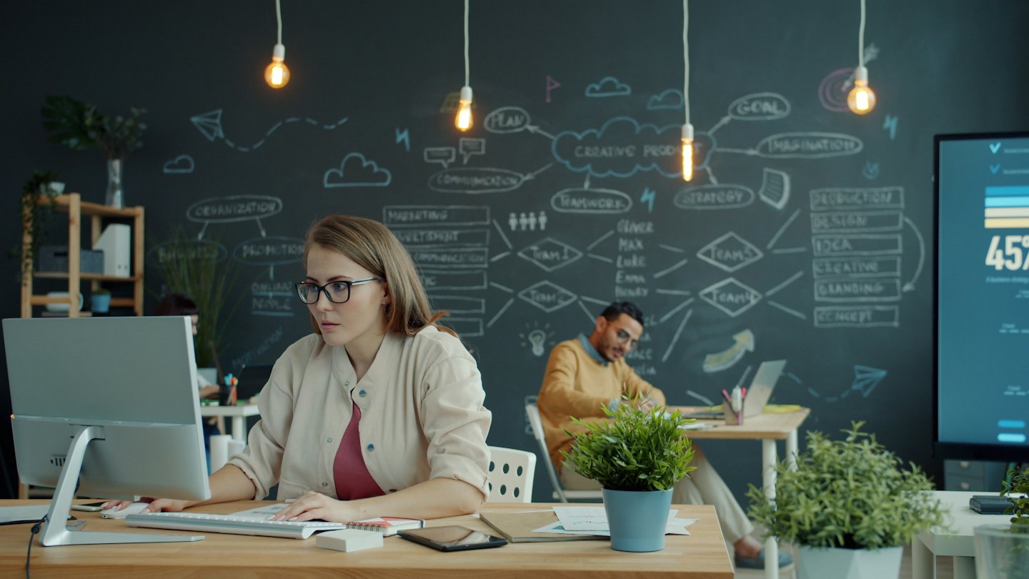 Woman works on computer with man in background in office.