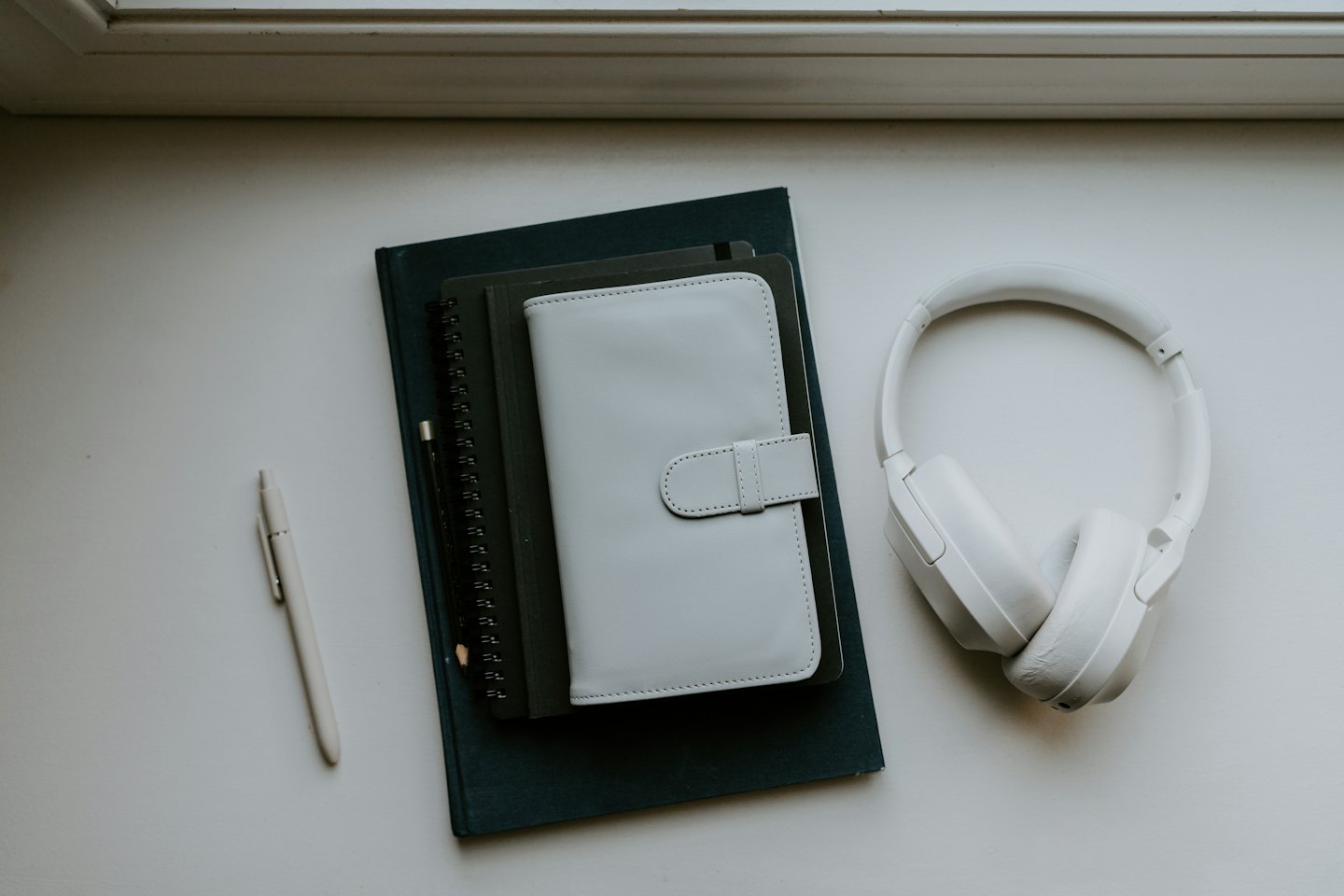Desk essentials including notebooks, planner, and headphones on white surface.